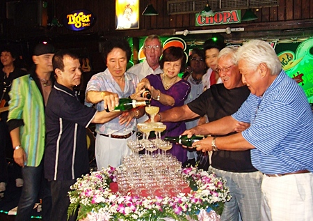 Diana Group Managing Director Sopin Thappajug, center, helps start the champagne waterfall as part of the 23rd anniversary celebrations for the Green Bottle Pub.